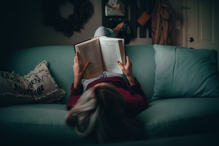 Girl Lying on a Couch Upside Down and Reading a Book
